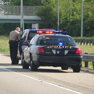 A police officer beside a patrol car on the highway, inspecting another vehicle - Law Office of E. Michael Linscheid.