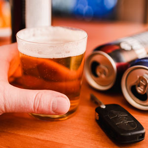 A person holds a beer glass beside a beer can and car key, illustrating the context of common DUI defenses. - Law Office of E. Michael Linscheid