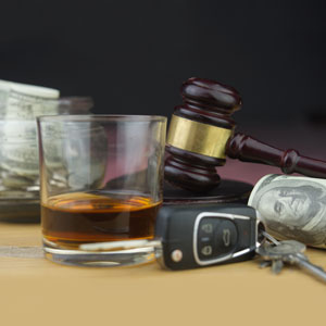 Glass of alcohol, car keys, cash, and a gavel, symbolizing DUI